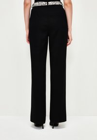 Pantalon large noir avec une ceinture noire et blanche à motifs. Texture de tissu lisse, design minimaliste, sans poches visibles.