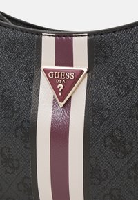 Section de sac texturée noire avec des rayures verticales bordeaux et blanches, avec un logo triangulaire Guess USA bordeaux avec un point d'interrogation.