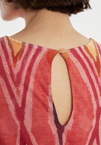 Robe à motif rouge avec une ouverture en forme de trou de serrure au dos, maintenue par un bouton rond. Tissu texturé avec un design abstrait vibrant.