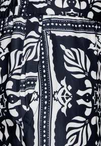 Zwart-wit gestreepte stof met gedurfde bloemmotieven en geometrische accenten. Gladde textuur met zichtbare stikdetails.