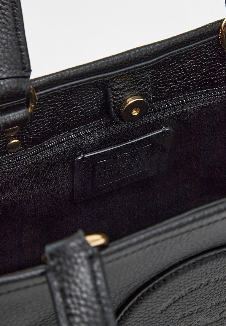 Interior de un bolso de cuero negro con textura suave, herrajes dorados, un bolsillo con cremallera y un bolsillo para tarjetas.