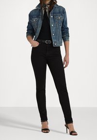 Denimjacka i blekt blått, svarta skräddarsydda jeans och svarta klacksandaler. Svart scarf med blommigt mönster runt halsen.