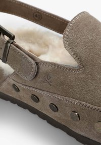 Sandalia de ante marrón con un interior suave, correa ajustable y herrajes metálicos. Presenta remaches redondos a lo largo del lateral y una etiqueta de talla 40.