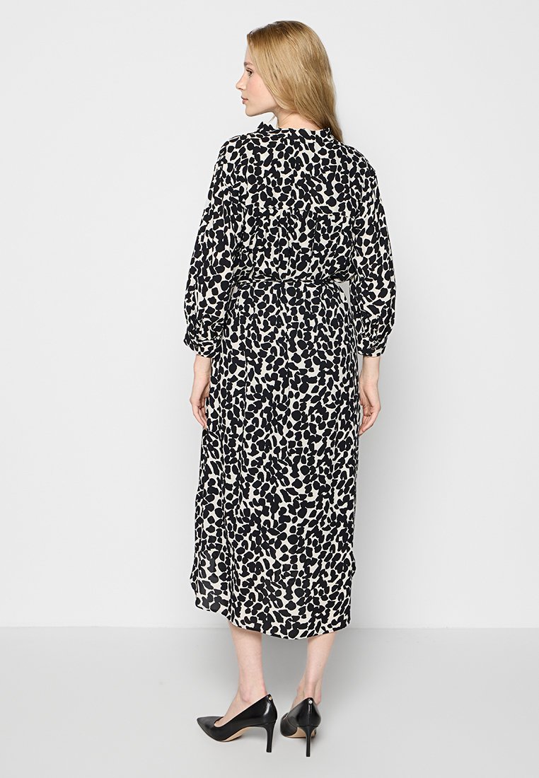 Schwarz-weißes Leopardenmuster-Maxikleid mit langen Ärmeln, tailliertem Schnitt und fließender Silhouette. Gestylt mit schwarzen High Heels.