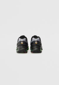 Baskets de sport noires et grises avec semelles en caoutchouc, accents verts et rouges, et une tige en mesh. Présente un logo à l'arrière et un design texturé.