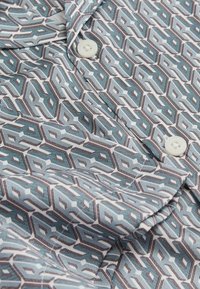 Cămașă cu mânecă scurtă, cu un model geometric în nuanțe de albastru, alb și maro, având o textură netedă și nasturi albi la guler.