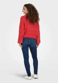 Rode gebreide trui met een textuurpatroon, cropped fit en brede mouwen, gecombineerd met donkerblauwe skinny jeans en witte schoenen.