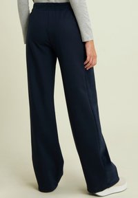 Pantaloni larghi color navy realizzati in tessuto morbido con una vestibilità rilassata, caratterizzati da una cintura liscia e una sottile texture sui pannelli laterali.