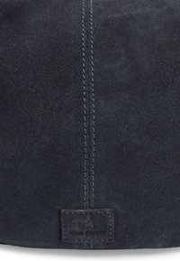 Tissu en daim bleu foncé avec surpiqûres doubles verticales et une petite étiquette de marque rectangulaire cousue au centre en bas.