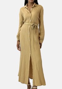 Lang, knappet kjole i struktureret beige stof, med lange ærmer, en taljebælte og et lige snit med en sideslids.