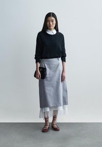 Czarny dzianinowy sweter, szara spódnica midi z koronkową lamówką, czerwone sznurowane buty oraz czarna torebka. Prosty design, warstwowe tekstury i neutralne kolory.