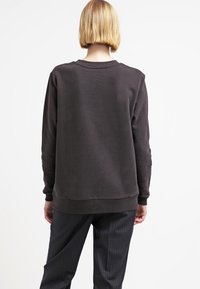 Felpa grigia scura, con collo girocollo, orlo e polsini a costine, texture liscia, vestibilità rilassata, indossata con pantaloni a righe.