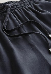 Pantaloni bleumarin cu șnur, confecționați dintr-un material texturat, cu talie adunată și două accente metalice argintii la capetele șnururilor.