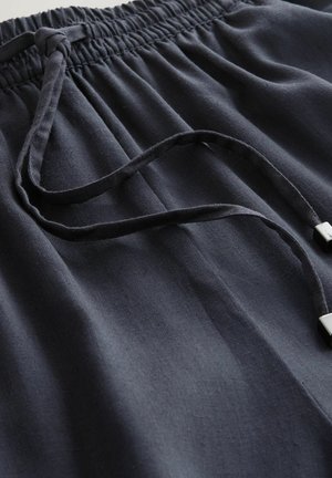 Tamsiai mėlynos spalvos raišteliu sutraukiamos kelnės, pagamintos iš tekstūruoto audinio, turinčios surinktą liemens juostą ir du sidabrinės spalvos metalinius galus ant raištelių.