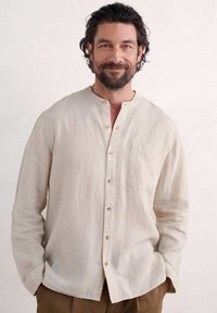 Beige linnen shirt met een bandkraag, voorpaspel en houten knopen. Voorzien van een borstzak en een relaxed fit.