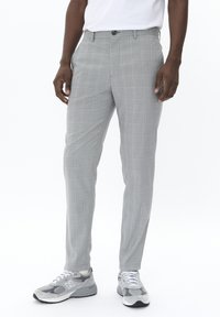Pantalones ajustados gris claro con un sutil patrón de cuadros, con cierre de botón y bolsillos; combinados con zapatillas grises.