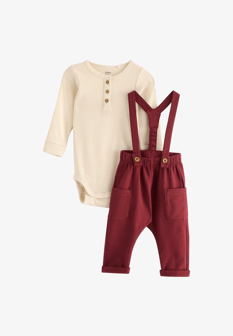 Beige gerippter Langarm-Body mit drei Knöpfen, kombiniert mit burgunderroten Jogginghosen mit verstellbaren Trägern und zwei Fronttaschen.