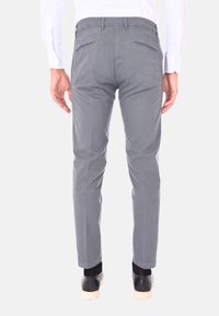 Pantaloni in cotone grigi con vestibilità slim, due tasche posteriori con cerniere e una superficie liscia. Abbinati a scarpe nere.