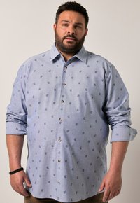 Camisa abotonada de color azul claro con un patrón de pequeños motivos en azul oscuro, con cuello clásico y botones marrones, mangas enrolladas.