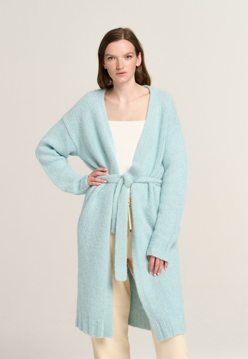 Light blue knitted cardigan with long sleeves, open front, and a tied waist. Features ribbed detailing at the cuffs and hem.