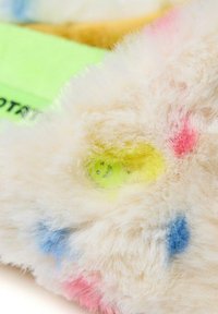 Juguete de peluche difuso con una base color crema, que presenta manchas coloridas en azul, rosa y verde. Superficie texturizada con brillantes acentos neón.