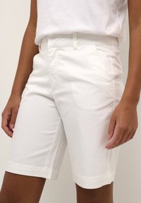 Pantaloni corti bianchi in cotone con una texture liscia, caratterizzati da un design a taglio dritto e risvolti, abbinati a una semplice maglietta bianca.