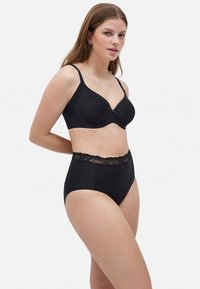 Sujetador negro de tela suave con copas moldeadas, combinado con braguitas negras de talle alto que presentan un bordado de encaje en la cinturilla.