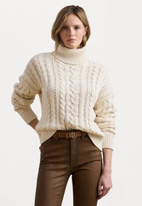 Dikke romige gebreide coltrui met kabelpatronen, gecombineerd met strakke bruine broek en een riem met een gouden "RL"-gesp.