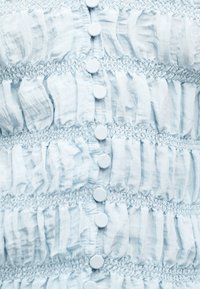 Ανοιχτό μπλε ύφασμα με κάθετες σειρές από μικρά στρογγυλά κουμπιά και ραμμένες ελαστικές λωρίδες που δημιουργούν υφασμένες οριζόντιες ρίγες.