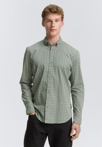 Chemise verte à boutons avec un motif abstrait blanc, manches longues et col classique. Fabriquée en tissu avec une texture lisse.