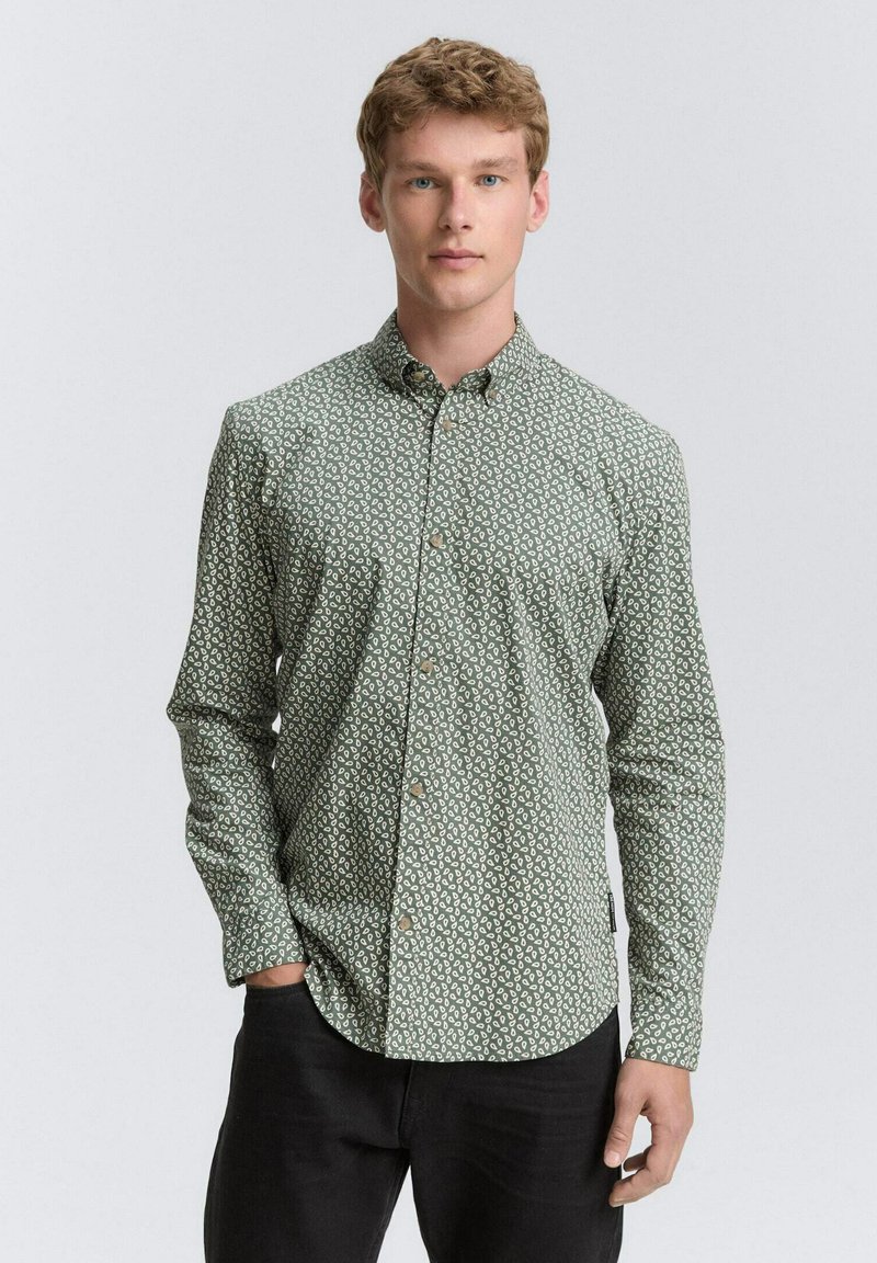 Chemise verte à boutons avec un motif abstrait blanc, manches longues et col classique. Fabriquée en tissu avec une texture lisse.