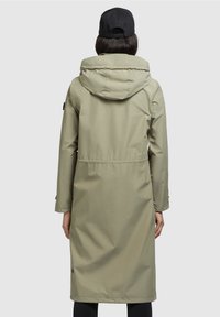 Veste imperméable longue de couleur vert olive avec capuche, taille élastique et coupe décontractée, dotée d'un seul patch logo sur la manche gauche.