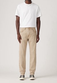Jeans de mezclilla de color beige claro con corte recto, combinados con una camiseta blanca lisa y zapatillas bajas negras. Diseño simple, sin patrones.
