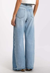 Vaqueros de pierna ancha azul claro hechos de mezclilla, con cintura alta, dobladillo deshilachado y dos bolsillos traseros. Textura suave con un ajuste relajado.