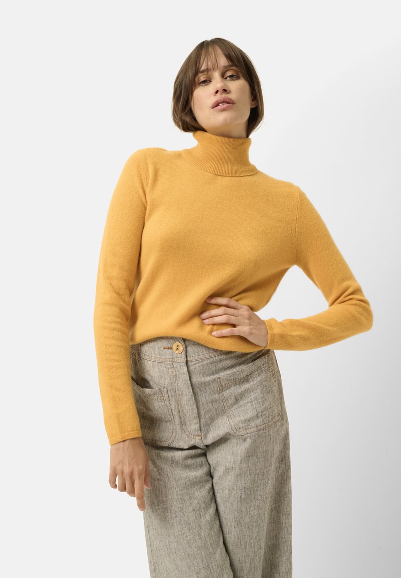Maglione a collo alto giallo realizzato in un tessuto morbido, con maniche lunghe e colletto a coste, abbinato a pantaloni grigi a vita alta con texture.