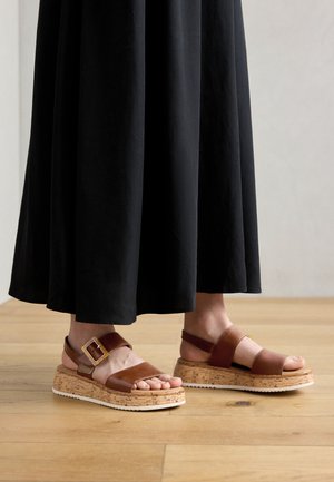 Rudos odinės šlepetės su kamštiniu padu. Pasižymi plačiu dirželiu ir sagtimi. Priderintos prie juodos sijono su glotnia tekstūra.