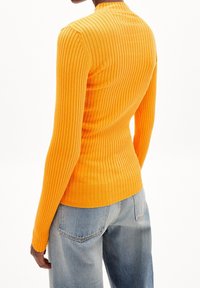 Haut à manches longues côtelé de couleur jaune éclatant, doté d'une coupe ajustée et d'un col montant. Associé à un jean bleu clair à coupe ample.