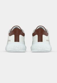 Λευκά αθλητικά παπούτσια με καφέ δερμάτινες λεπτομέρειες στη φτέρνα, με στιλβωμένη λευκή σόλα που φέρει το ανάγλυφο γράμμα 'VALENTINO' στο πλάι.