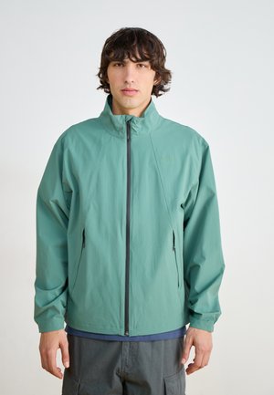 Lightweight, mint-green jacket with a high collar, zip front, and two side pockets; smooth texture and minimalist design.