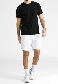 Svart kortärmad t-shirt med rund hals och grön logotyp, kombinerad med vita shorts och vita sportskor. Slät tygstruktur.
