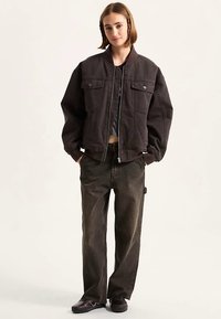 Black bomber jacket with two front pockets, ribbed collar, and zipper closure. Paired with dark, loose-fitting jeans and black shoes.