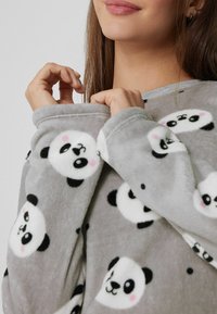 Prenda de forro polar gris con patrón de cara de panda, con textura suave, mangas largas y detalles en los puños. Diseño cómodo y casual.