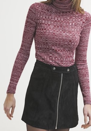 Kobieta ubrana w teksturowany bordowy sweter z golfem oraz czarną mini spódniczkę zamszową z przednim zamkiem błyskawicznym i zatrzaskami.