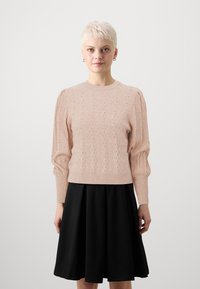 Svetlo roza, teksturiran pulover z valovitim vzorcem in rebrastimi manšetami, v kombinaciji s črno krilom s flared krojem. Okrogli ovratnik, srednja dolžina puloverja.