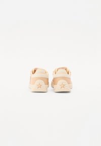Beige spordijalatsid siledast materjalist, millel on taga tähte kujutav aktsent ja kontrastne valge kand. Minimalistlik disain pehmeid kõveraid.