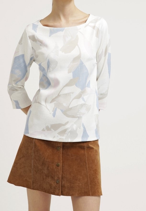 Witte top met abstracte lichtblauwe en grijze bladerenpatronen, driekwart mouwen, gecombineerd met een bruine suède minirok met knoopdetails.