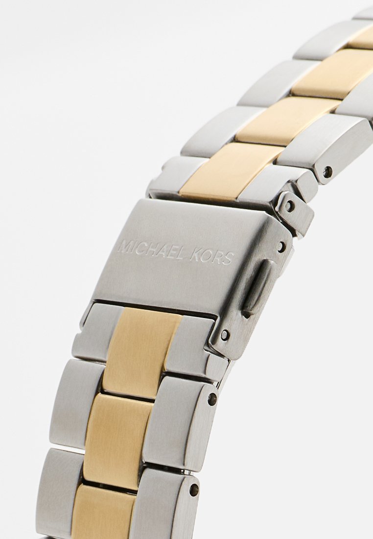 Montre en métal avec un bracelet en argent et en or. Présente un fermoir rectangulaire gravé "MICHAEL KORS". Les maillons affichent une finition lisse et polie.