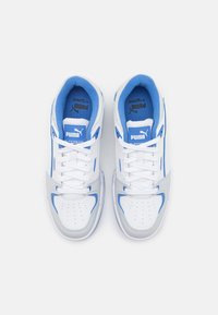 Paire de baskets Puma Slipstream blanches et bleues avec lacets, vues de dessus sur un fond blanc uni.