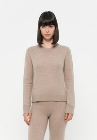 Beige kasjmirgenser med rund hals, ribbede ermer og kant. Myk tekstur og avslappet passform, kombinert med matchende bukser.