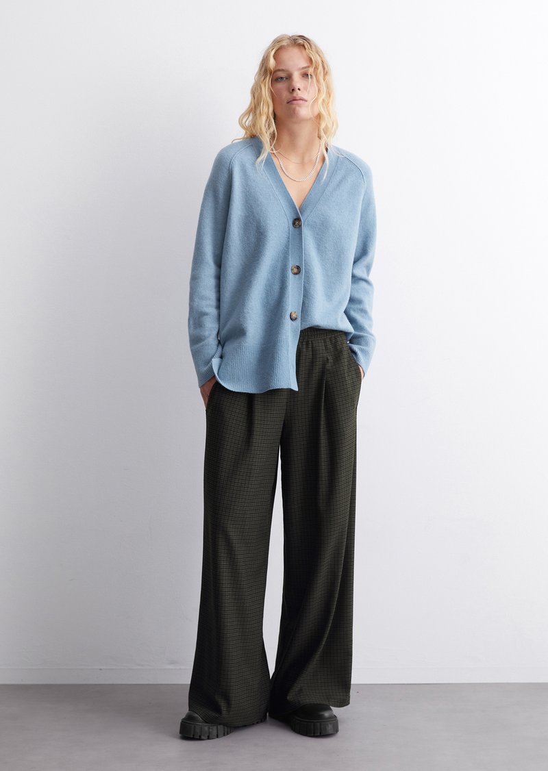 Hellblauer Cardigan mit V-Ausschnitt und fünf Knöpfen. Lockere, dunkel gemusterte Hose mit weitem Bein. Strukturierter Strickstoff.